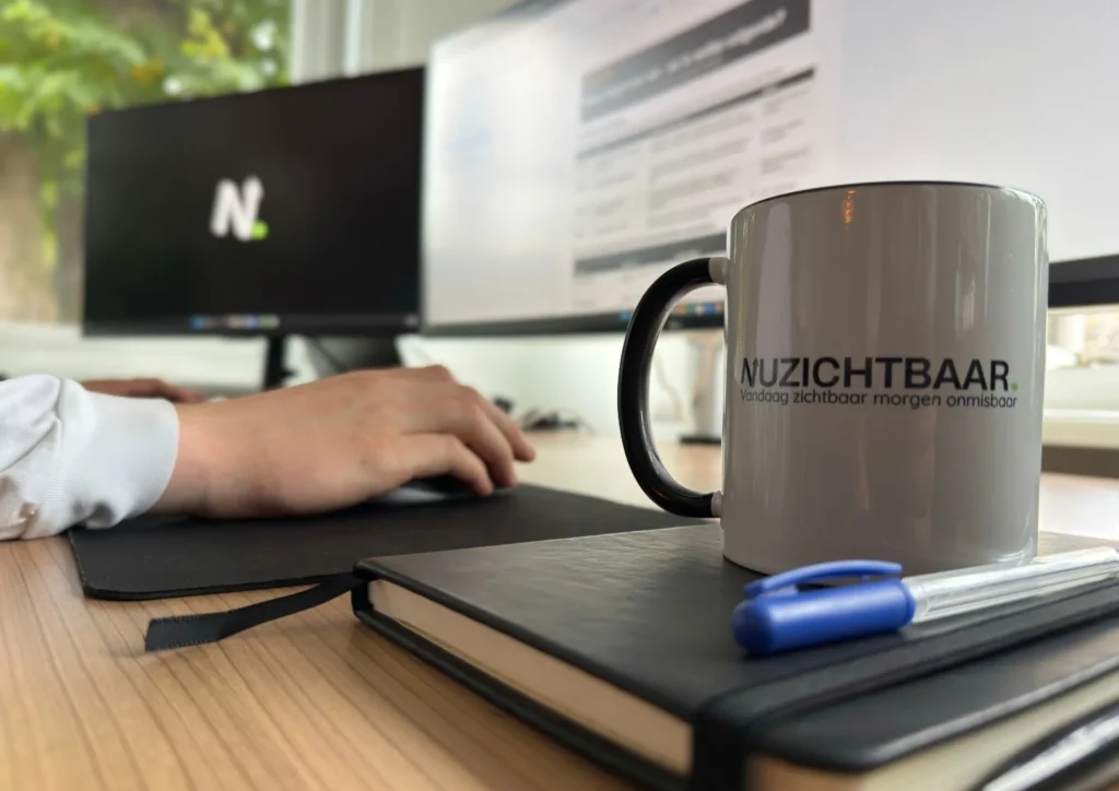 Werkplek bij Nuzichtbaar met mok en notitieboek naast het toetsenbord